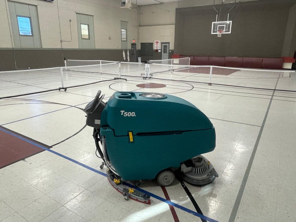 PowerKleen Tennant T500 commercial floor scrubber machine inside an indoor gymnasium and pickleball court facility.
