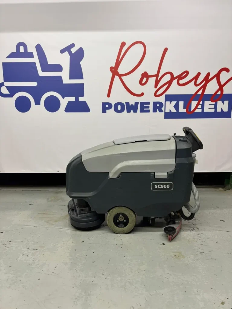 Side profile of an Advance SC900 walk-behind floor scrubber positioned in front of a Robeys PowerKleen backdrop inside a commercial equipment showroom.
