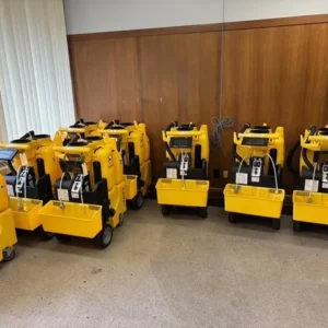 Multiple yellow Kaivac no-touch cleaning machines arranged inside a room, equipped with recovery trays, hose systems, and transport wheels for commercial restroom and facility cleaning operations.