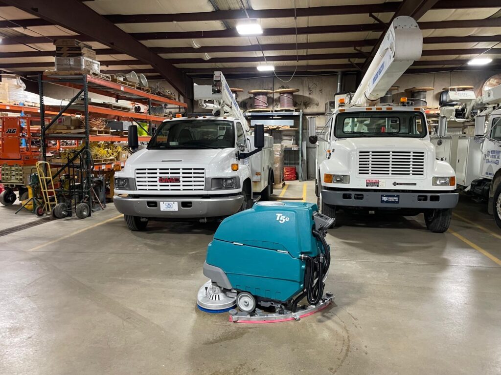 Indianapolis transport team members posing with a Tennant ride-on floor scrubber inside a large industrial facility during a commercial floor cleaning operation.